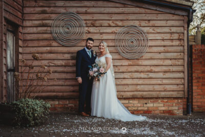 Wedding couple posing by wooden wall with spirals.