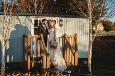 Bride and groom embracing in sunlight by cabin.