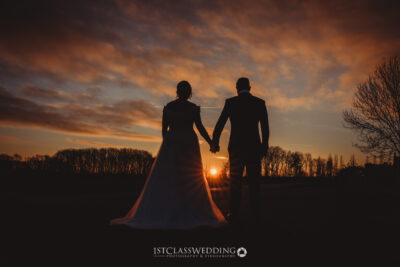 Couple holding hands at sunset wedding.