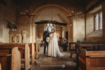 Bride and groom smiling in historic church aisle.