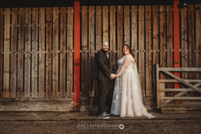 Couple posing in wedding attire by wooden barn.