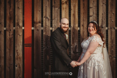 Bride and groom holding hands, wooden background.
