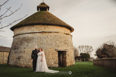 Couple by historic stone dovecote, wedding day.
