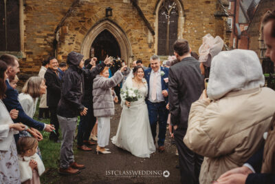 Joyful wedding couple with confetti exiting church.