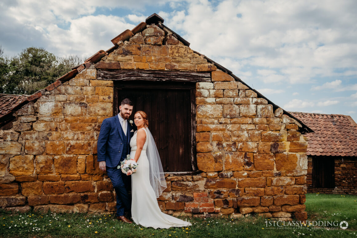 Bride and groom posing by old stone building.