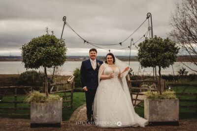 Bride and groom smiling outdoors, waterfront wedding venue.