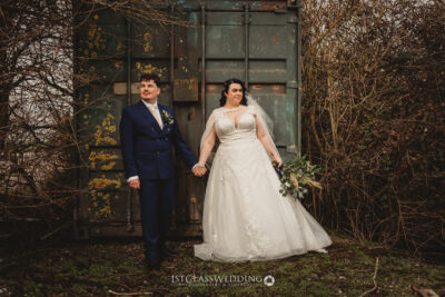 Bride and groom holding hands in industrial setting.