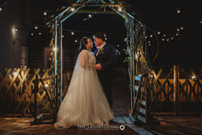 Couple under lit archway at night wedding.
