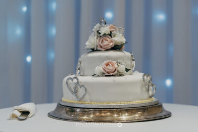 Elegant two-tier wedding cake with roses and hearts decoration.