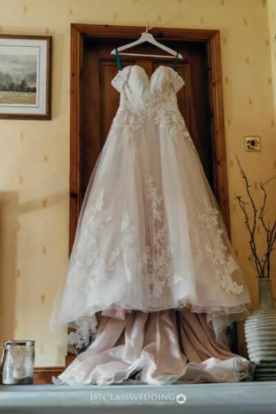 Elegant bridal gown hanging in room with countryside view.