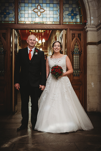 Bride and groom smiling in historic building aisle.
