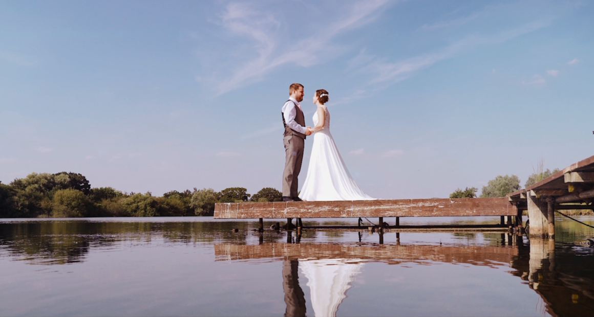 Bride and groom standing on jetty by lake