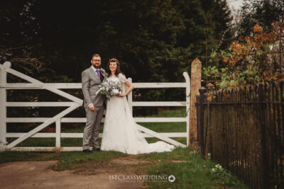 Bride and groom by rustic gate, countryside wedding.