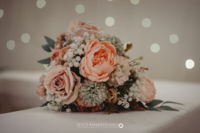 Elegant peach wedding bouquet with bokeh lights background.