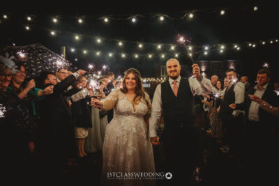 Bride and groom with sparklers at evening wedding celebration.