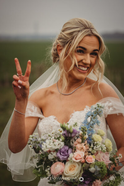Bride gesturing peace sign with bouquet.