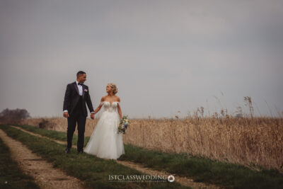Couple walking hand in hand in countryside wedding.