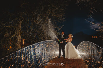 Couple with champagne on illuminated bridge at night.
