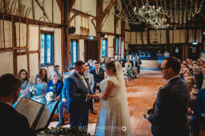 Wedding ceremony in rustic hall with guests watching at Kingfisher Tithe Barn Wedding Venue Bedford.