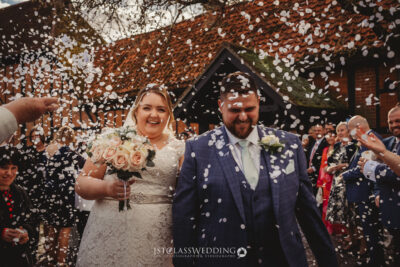 Couple smiling under shower of confetti at Kingfisher Tithe Barn Wedding Venue Bedford.