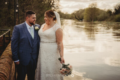 Wedding couple by river at sunset at Kingfisher Tithe Barn Wedding Venue Bedford.