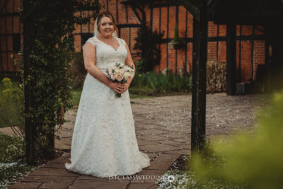 Bride with bouquet in garden setting at Kingfisher Tithe Barn Wedding Venue Bedford..