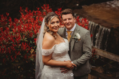 Bride and groom posing by waterfall with red foliage.