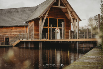 Couple on wooden lodge balcony over water outside Mill Barns wedding venue