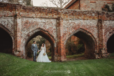 Couple posing at historical brick archway on wedding day at Hedingham Castle.