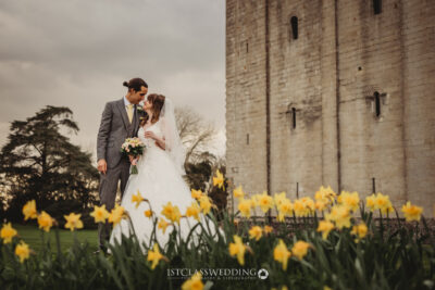 Bride and groom embracing near castle, spring daffodils in foreground at Hedingham Castle.