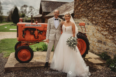 Bride and groom posing by vintage tractor at wedding.