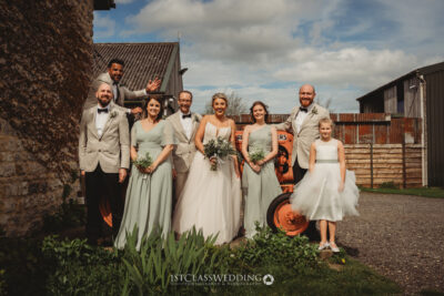 Wedding party posing outdoors with rustic backdrop.