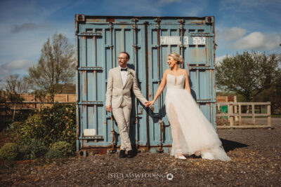 Bride and groom laughing by blue shipping container.