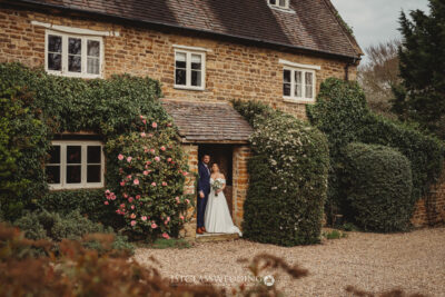 Couple posing at quaint stone cottage with ivy.