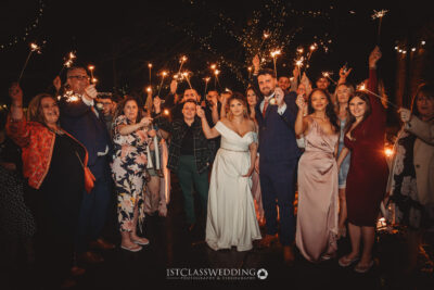 Wedding guests holding sparklers at night celebration.
