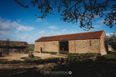 Rustic stone barn under blue sky with surrounding greenery at Dodfrod Manor