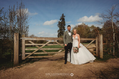 Bride and groom smiling outdoors by wooden gate.