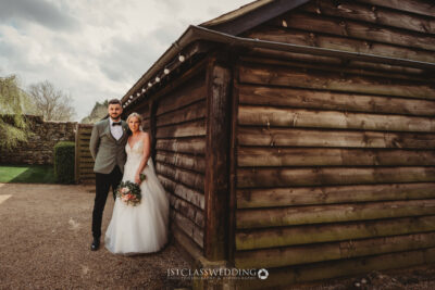 Bride and groom posing by wooden cabin outdoors.