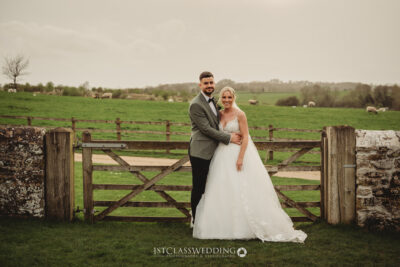 Bride and groom smiling in countryside field with sheep and lambs.